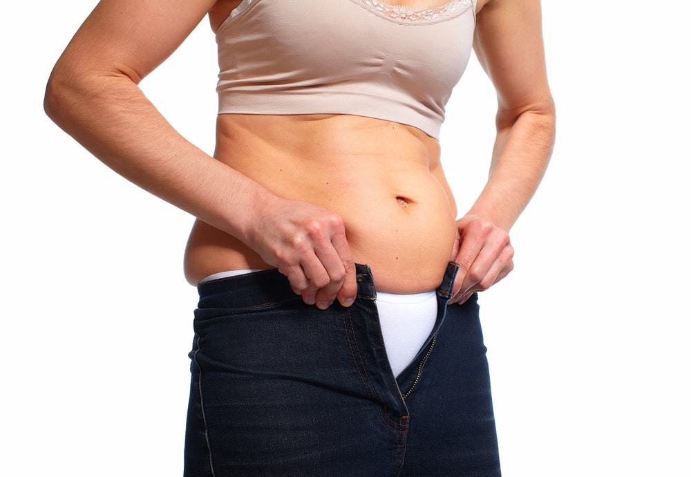 A woman struggling to button her jeans before getting a tummy tuck in Lewisville