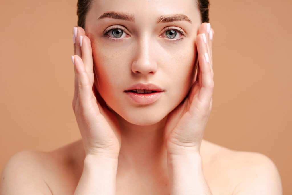 Woman touching her face with visible redness on one cheek, illustrating skin concerns treated with IPL photofacial and laser resurfacing.