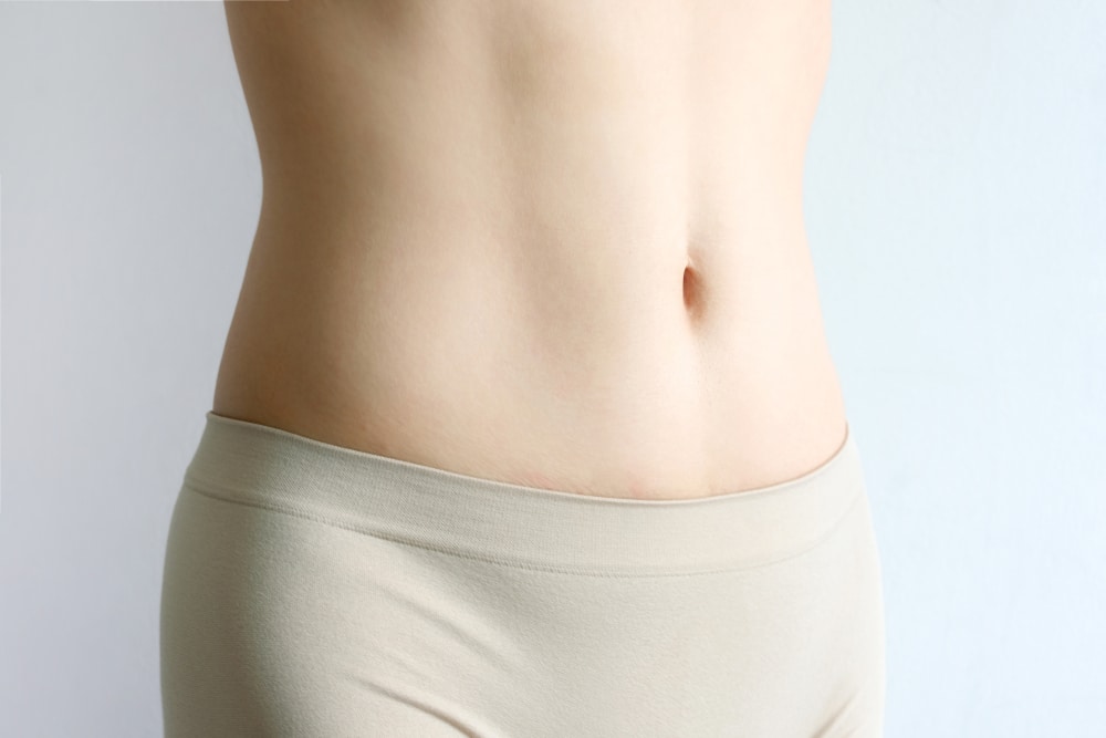 A woman looking in the mirror and considering differences between upper and lower eyelid surgery Cropped shot of a woman's stomach after a tummy tuck in Lewisville