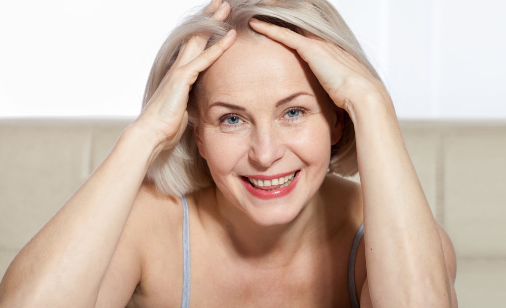 A woman looking in the mirror and considering differences between upper and lower eyelid surgery Woman smiling after a facelift in Lewisville, TX