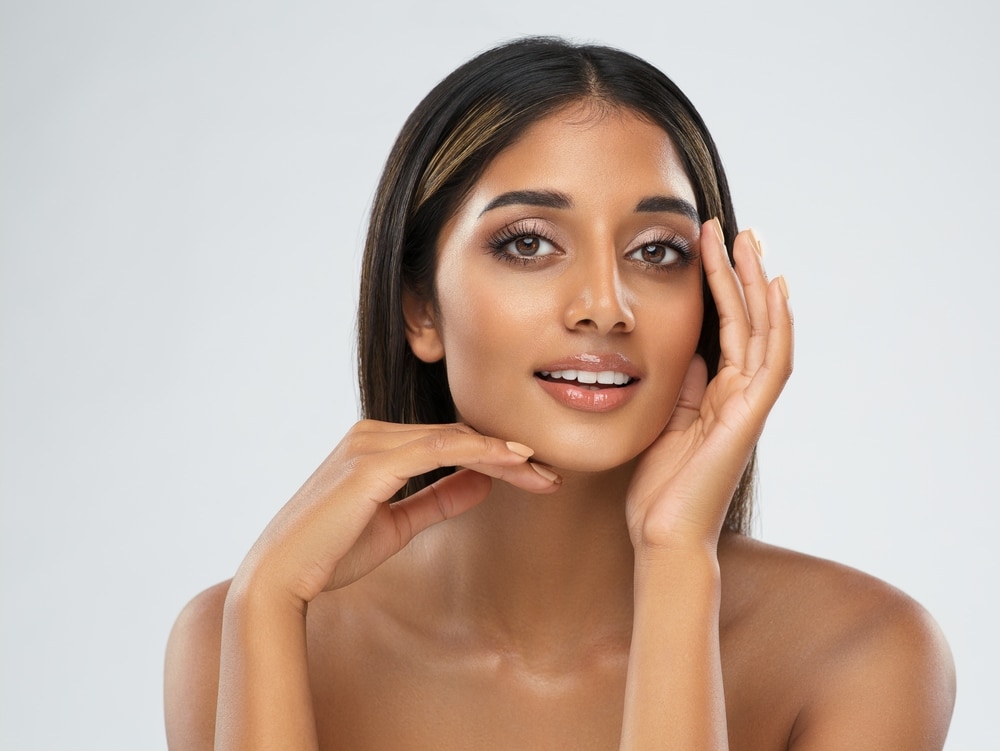 A woman looking in the mirror and considering differences between upper and lower eyelid surgery Woman smiling and showing the results of Sculptra in Lewisville